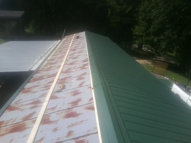 Old rusted panels beside newly installed green metal roofing — Wind Damage Roof Repair by Roofing Brothers in Marquette