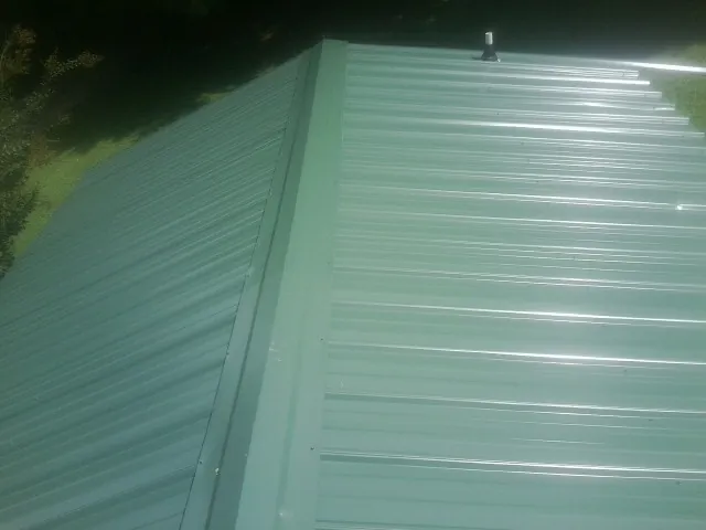 New green metal panels meeting at the ridge of a roof — Flat Roof Repair work by our crew in Marquette