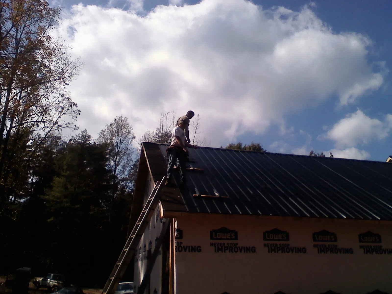 Roofer fastening dark metal panels high against a cloudy sky, from a Roof Inspection job in Marquette