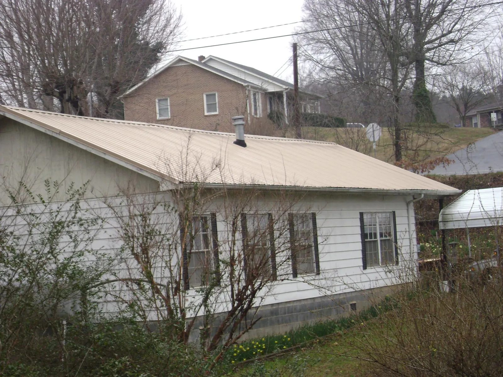Tan metal roof on a white sided house set into a hillside — Commercial Roofing by Roofing Brothers in Marquette